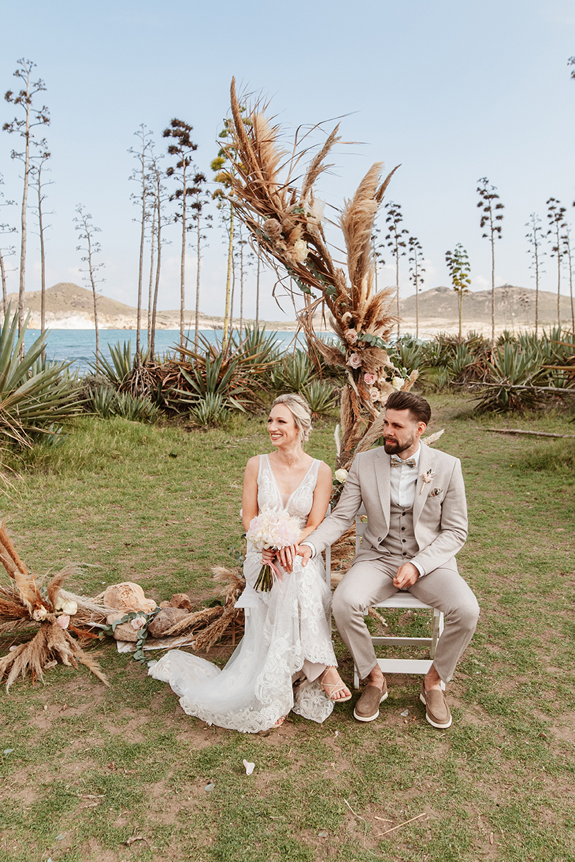 Brautpaar sitzt am Traubogen aus Trockenblumen, Hochzeit am Strand in Spanien, Cabo de Gata