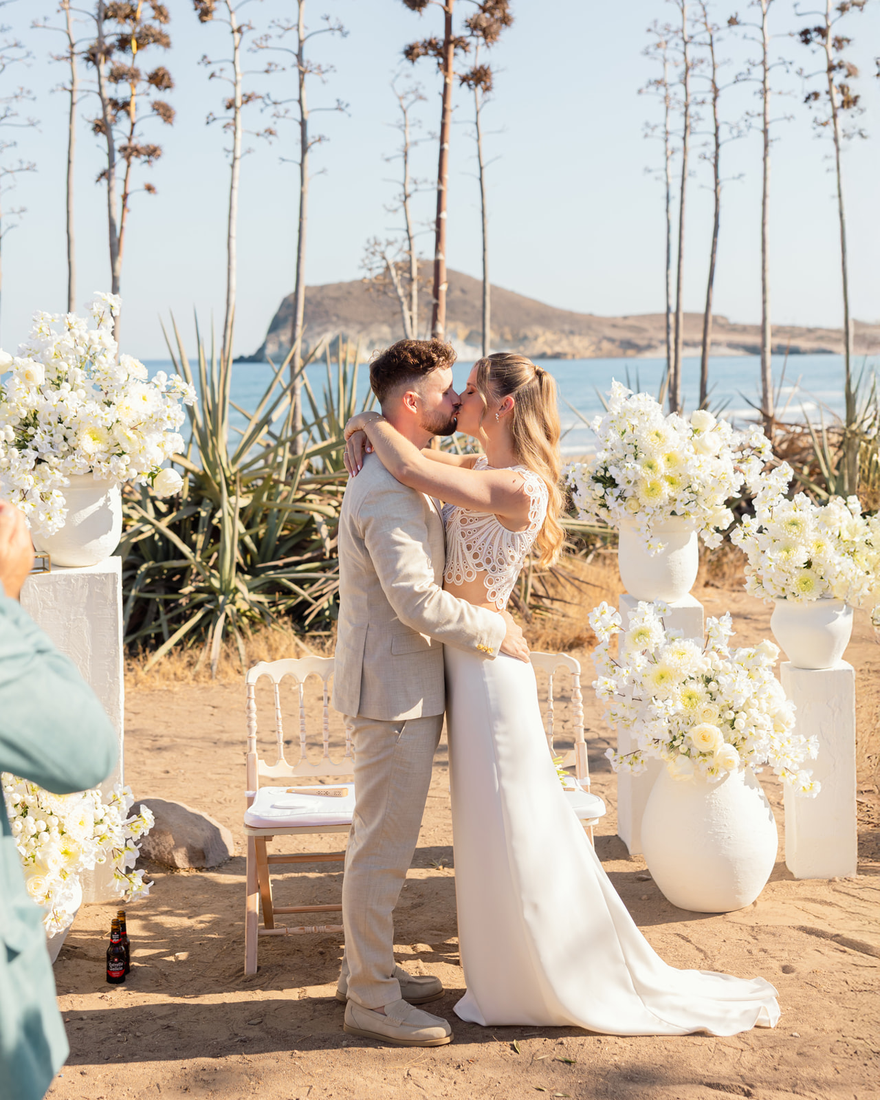 Erster Kuss als Ehepaar am Strand-Altar von San Jose - weisses Blumendekor, Agaven und tuerlaisblaues Meer von Cabo de Gata