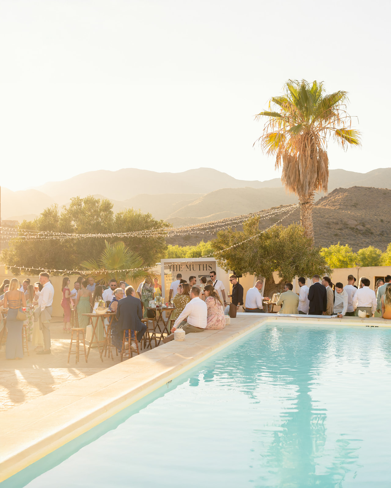 Aperitivo am Pool des Cortijo El Sotillo im Abendrot - The Muths Schild, Palme, Lichterketten, Berge von Almeria im goldenen Licht