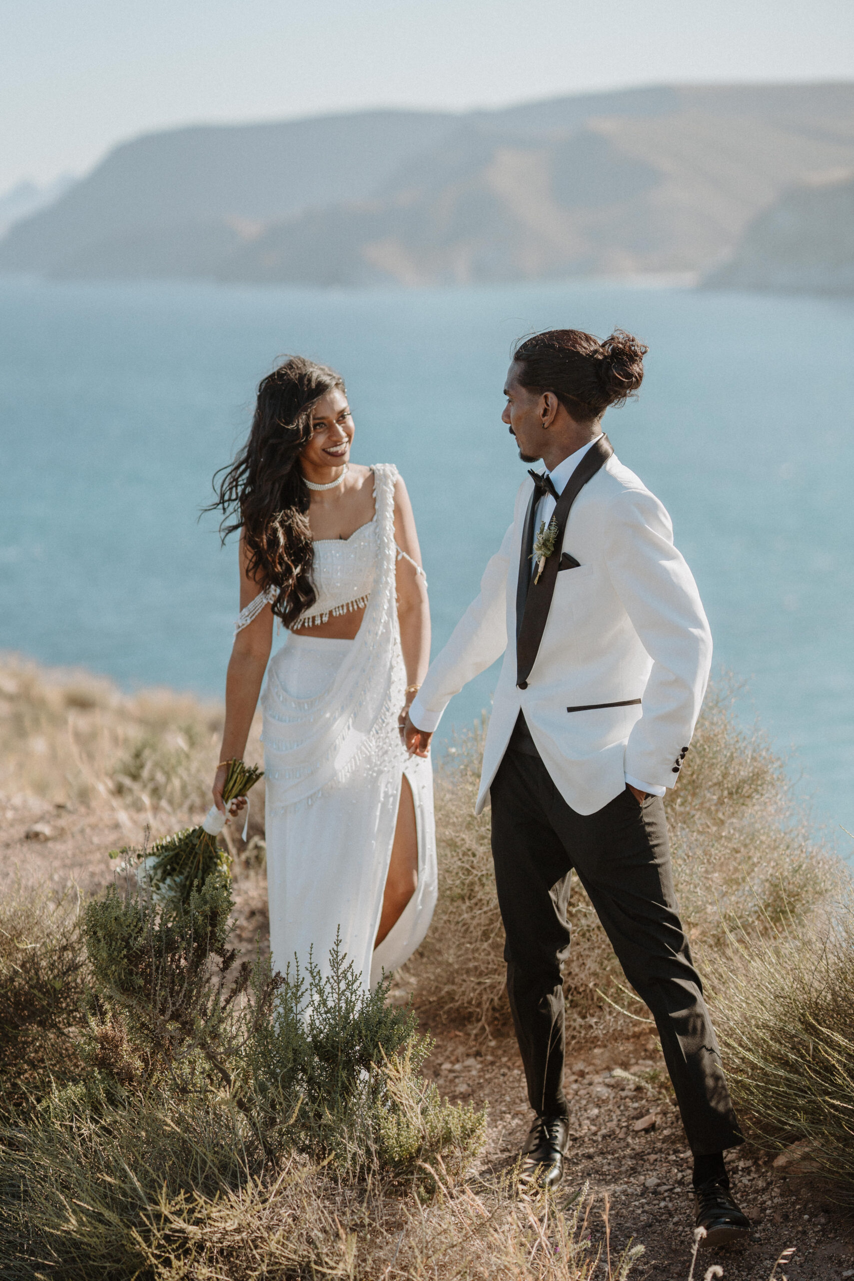 Brautpaar hält Hände auf der Klippe mit Meerblick, Destination Wedding Andalusien