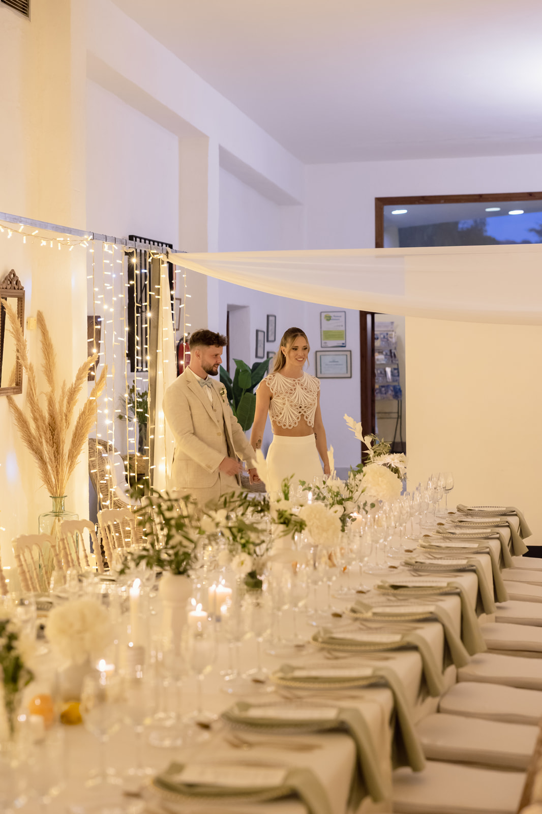 Katharina und Roman gehen am gedeckten langen Tisch entlang, Pampasgras und fallende Lichterketten, Dinner Cortijo El Sotillo