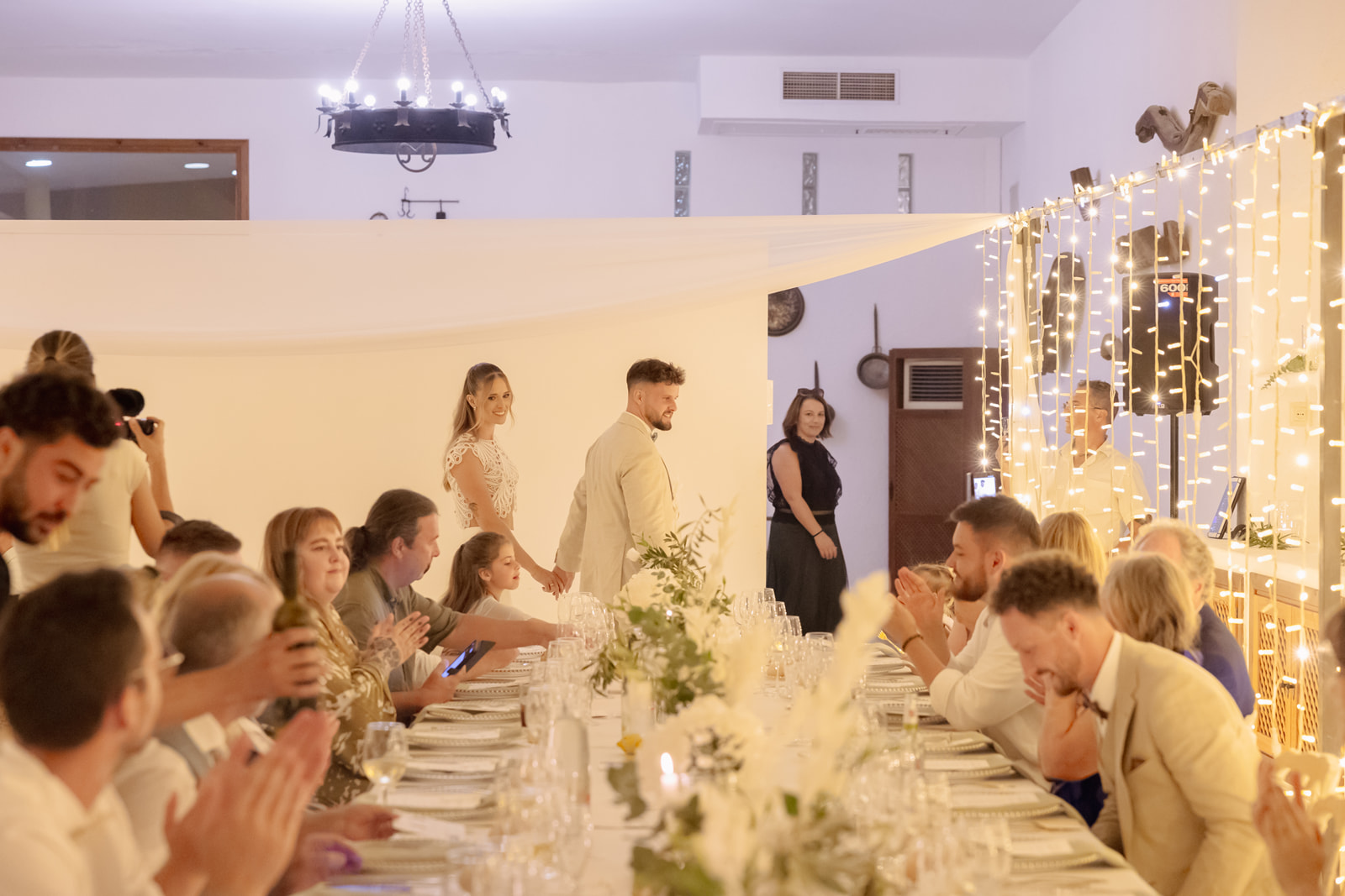 Gaeste klatschen beim Einzug von Katharina und Roman in den Dinnerraum, Lichterketten, Blumendekor, Cortijo El Sotillo