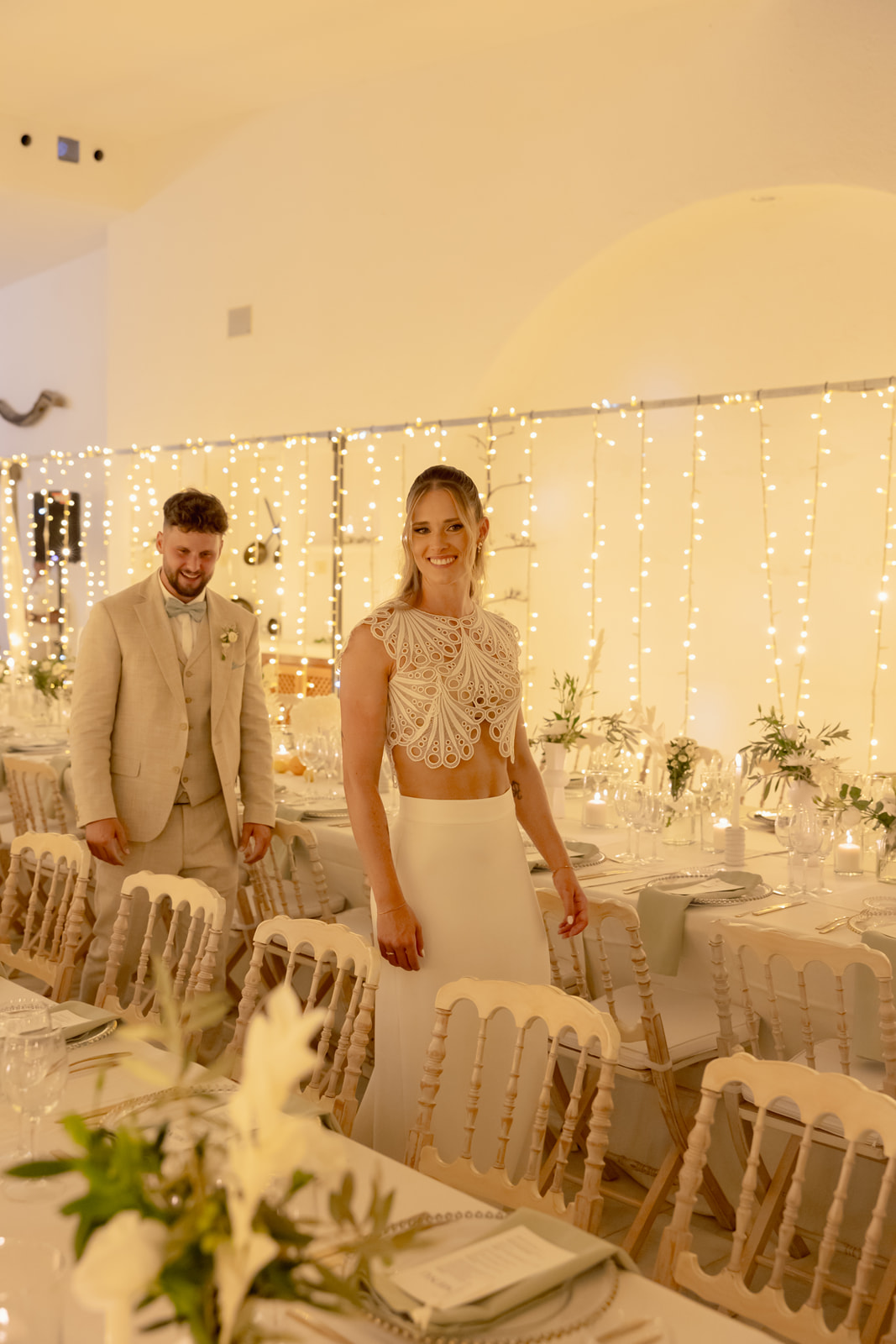 Katharina laechelt strahlend im warmen Licht des Dinnerraums, Lichterketten-Vorhang, Roman im Hintergrund, Hochzeit San Jose Spanien