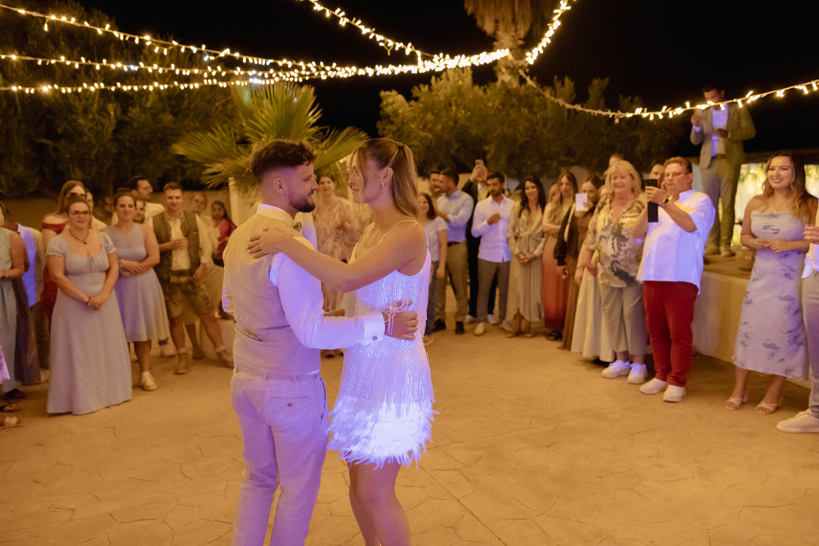 Katharina im weissen Fransen-Partykleid beim ersten Tanz mit Roman draussen unter Lichterketten, Nacht Cortijo El Sotillo