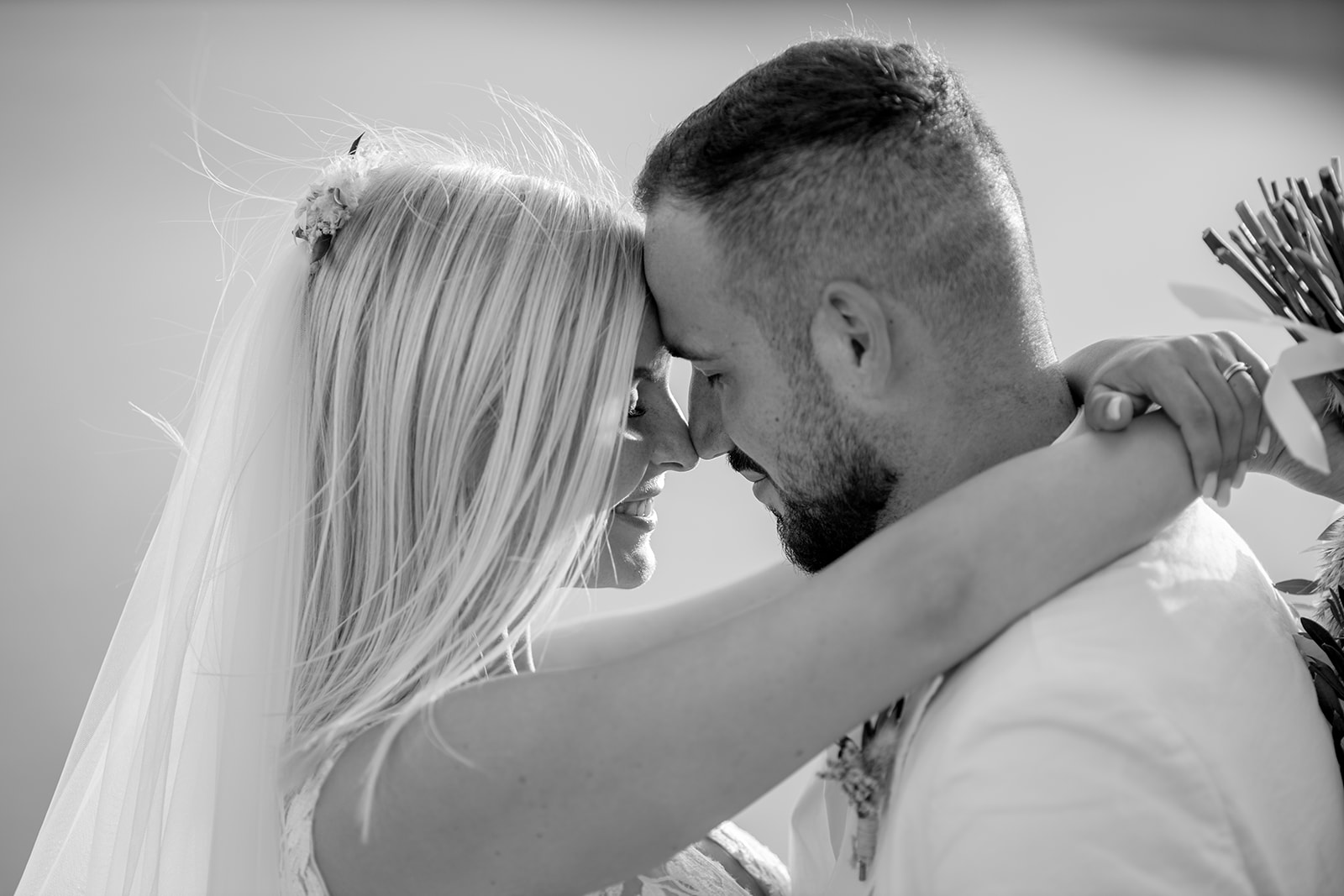 Schwarz-Weiß Hochzeitsportrait: Lara und Michael Stirn an Stirn, Schleier weht im Wind