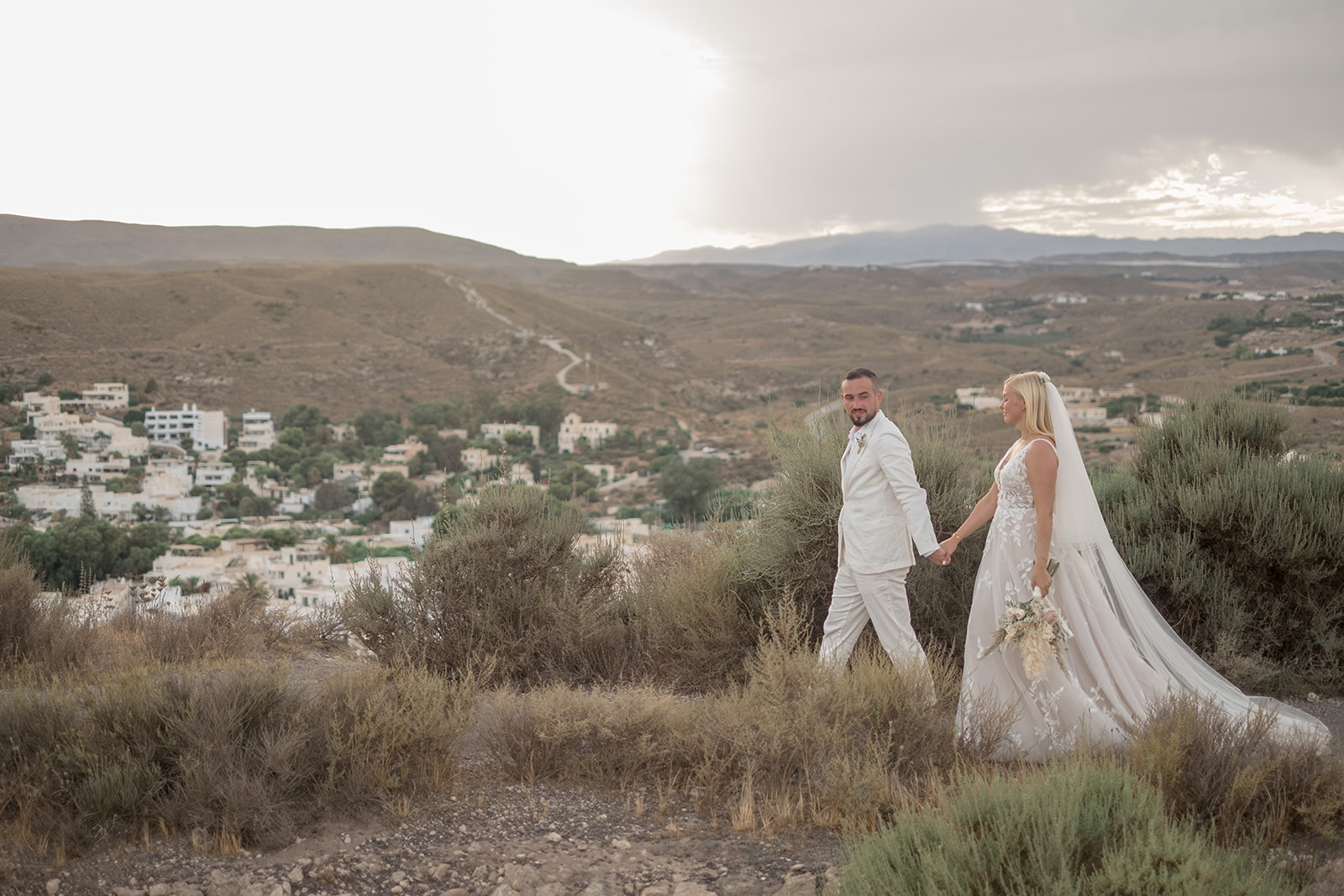 Lara und Michael gehen Hand in Hand über den Felskamm, dramatischer Wolkenhimmel, Naturpark Cabo de Gata