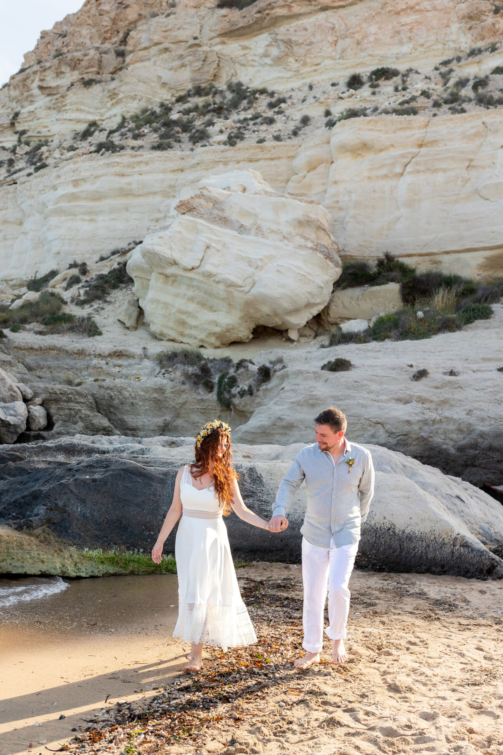 Brautpaar läuft Hand in Hand vor den Sandsteinfelsen am Strand, Agua Amarga, Boho Strandhochzeit Cabo de Gata