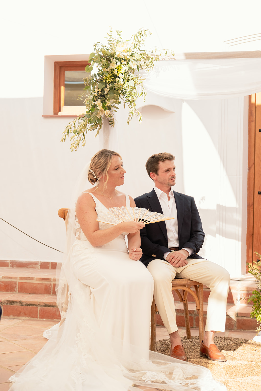 Brautpaar sitzt bei der freien Trauung unter dem Blumenbogen, Braut mit Fächer, Mojácar, Finca Hochzeit Andalusien