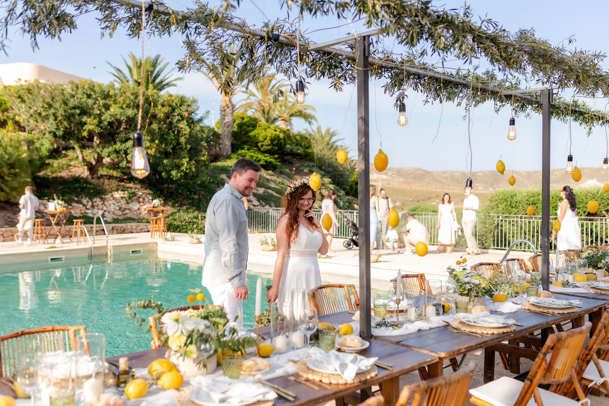 Brautpaar an der langen Hochzeitstafel mit hängenden Zitronen am Pool, Cabo de Gata, Boho Strandhochzeit