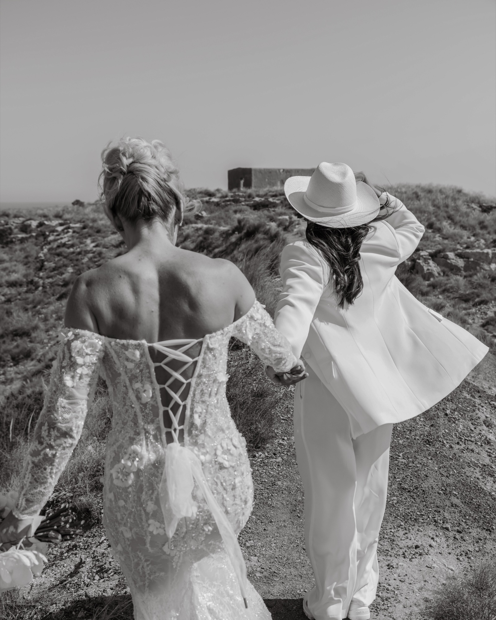 Zwei Bräute von hinten Hand in Hand, Spitzenkleid mit Schnürrücken, Cabo de Gata, Schwarzweiß