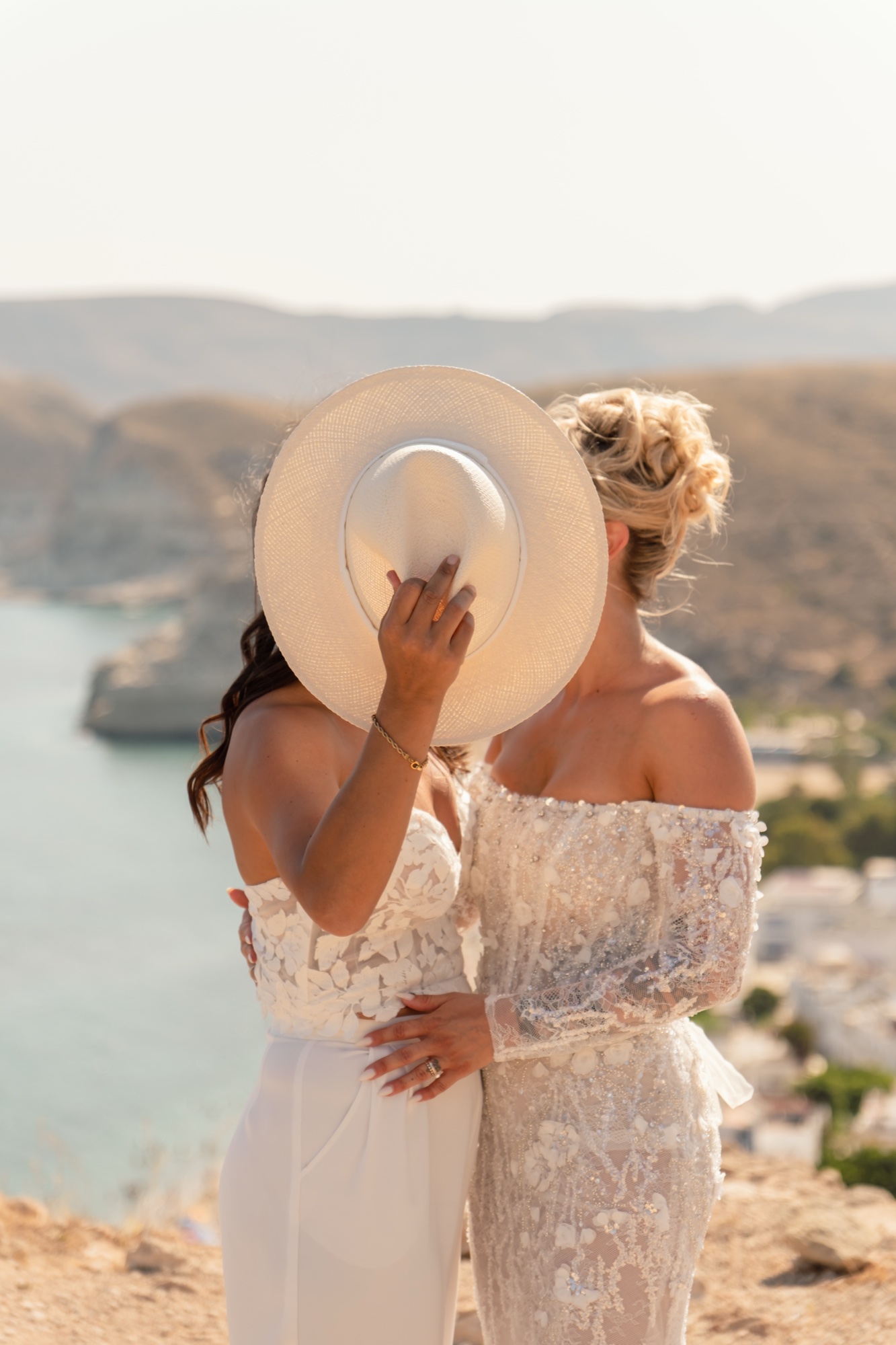 Die beiden Bräute küssen sich hinter einem Panamahut, Cabo de Gata, gleichgeschlechtliche Hochzeit in Spanien