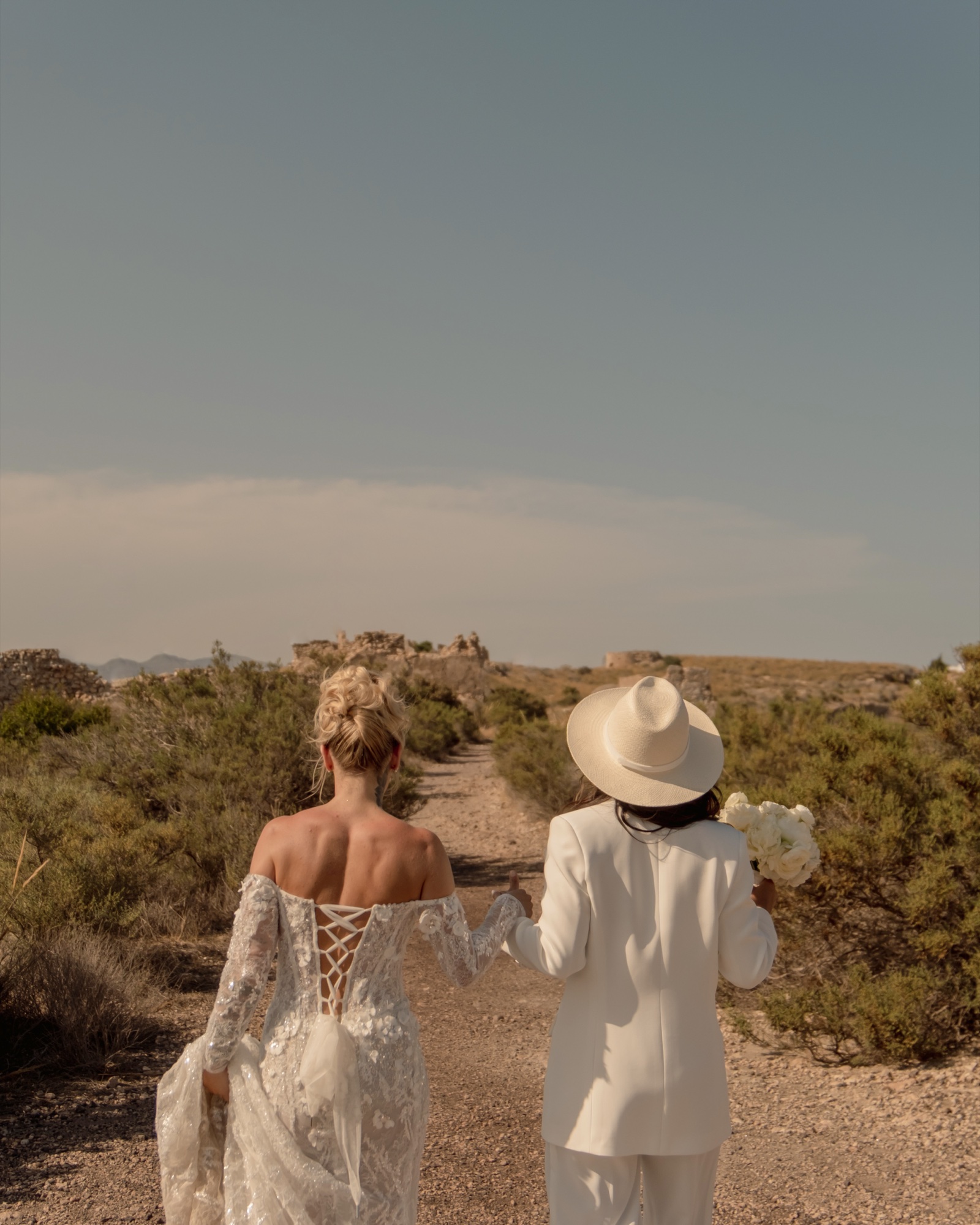 Zwei Bräute auf einem Sandweg durch die Wüstenlandschaft, Cabo de Gata Almería, Destination Wedding