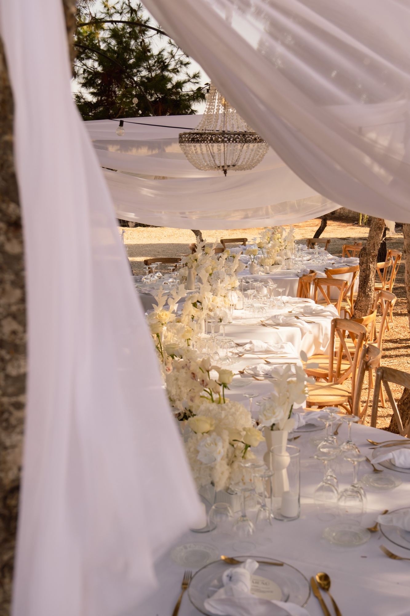 Blick durch weiße Stoffbahnen auf die Hochzeitstafel mit Kristalllüster, Location 17 Cabo de Gata, Hochzeit ganz in Weiß