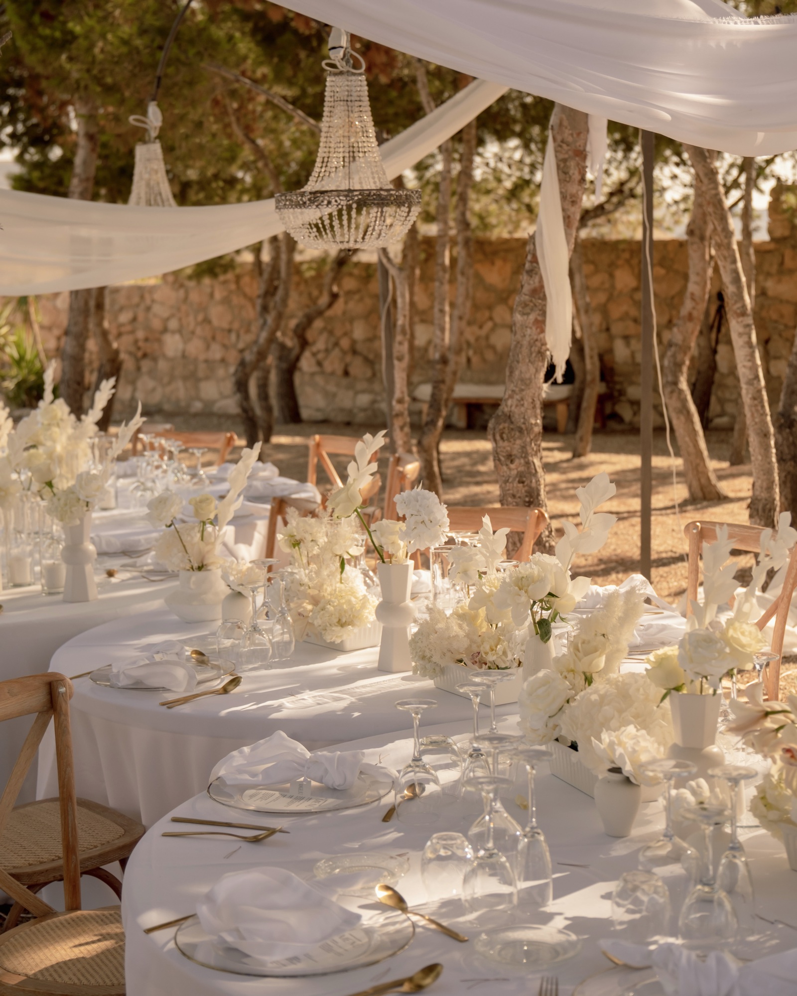 Lange weiß gedeckte Tafel unter Pinien mit Kristalllüstern, Location 17 Cabo de Gata, Hochzeit ganz in Weiß