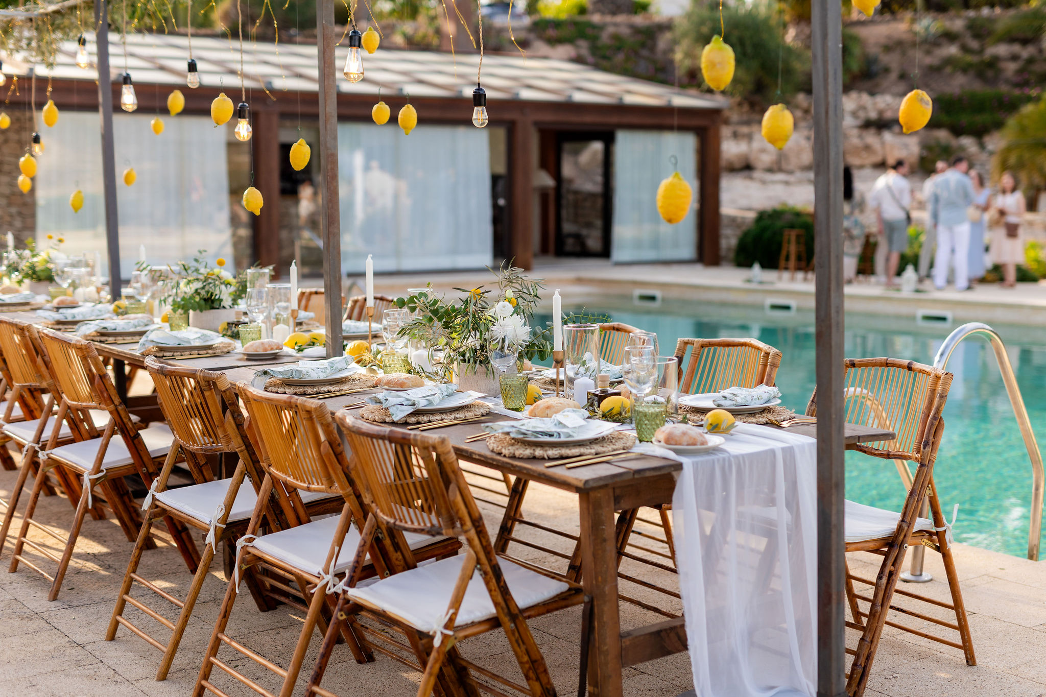 Lange Hochzeitstafel am Pool mit hängenden Zitronen und Lichterketten, Boho Strandhochzeit Cabo de Gata