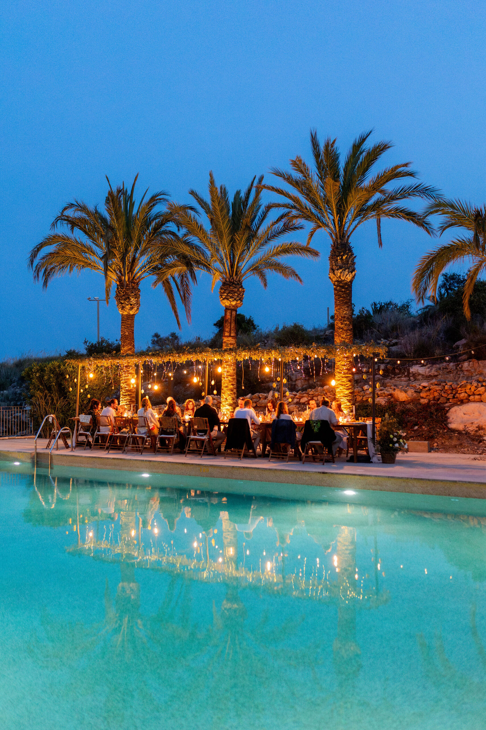 Beleuchtete Palmen und Pool in der blauen Stunde, die Tafel im warmen Licht, Agua Amarga, Boho Strandhochzeit Cabo de Gata