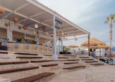 Überdachte Terrasse der Beachbar mit Rattanlampen und Blick über den Strand