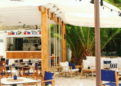 Terrasse des Chiringuito mit weißen Sonnensegeln und blauen Regiestühlen