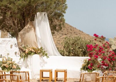 Traubogen aus wehendem Stoff zwischen weißen Mauern und Bougainvillea über dem Meer