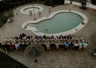Hochzeitsgesellschaft an langen Tafeln rund um den geschwungenen Pool, von oben fotografiert