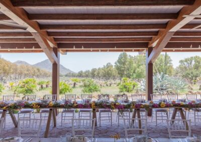 Lange Hochzeitstafel unter der offenen Holzpergola mit Blick über die Ebene