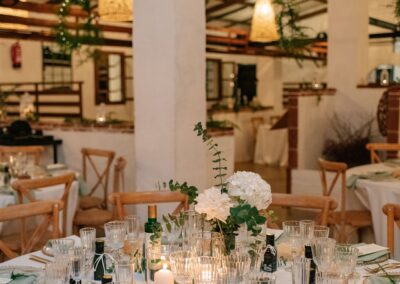 Runde Hochzeitstische im Saal der Finca mit hängenden Lampen und Grün