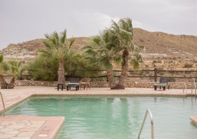 Pool der Finca über Agua Amarga tagsüber, dahinter Palmen und trockene Hügel