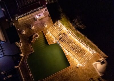Luftaufnahme der Hochzeit bei Nacht: Lichterketten und beleuchteter Pool von oben