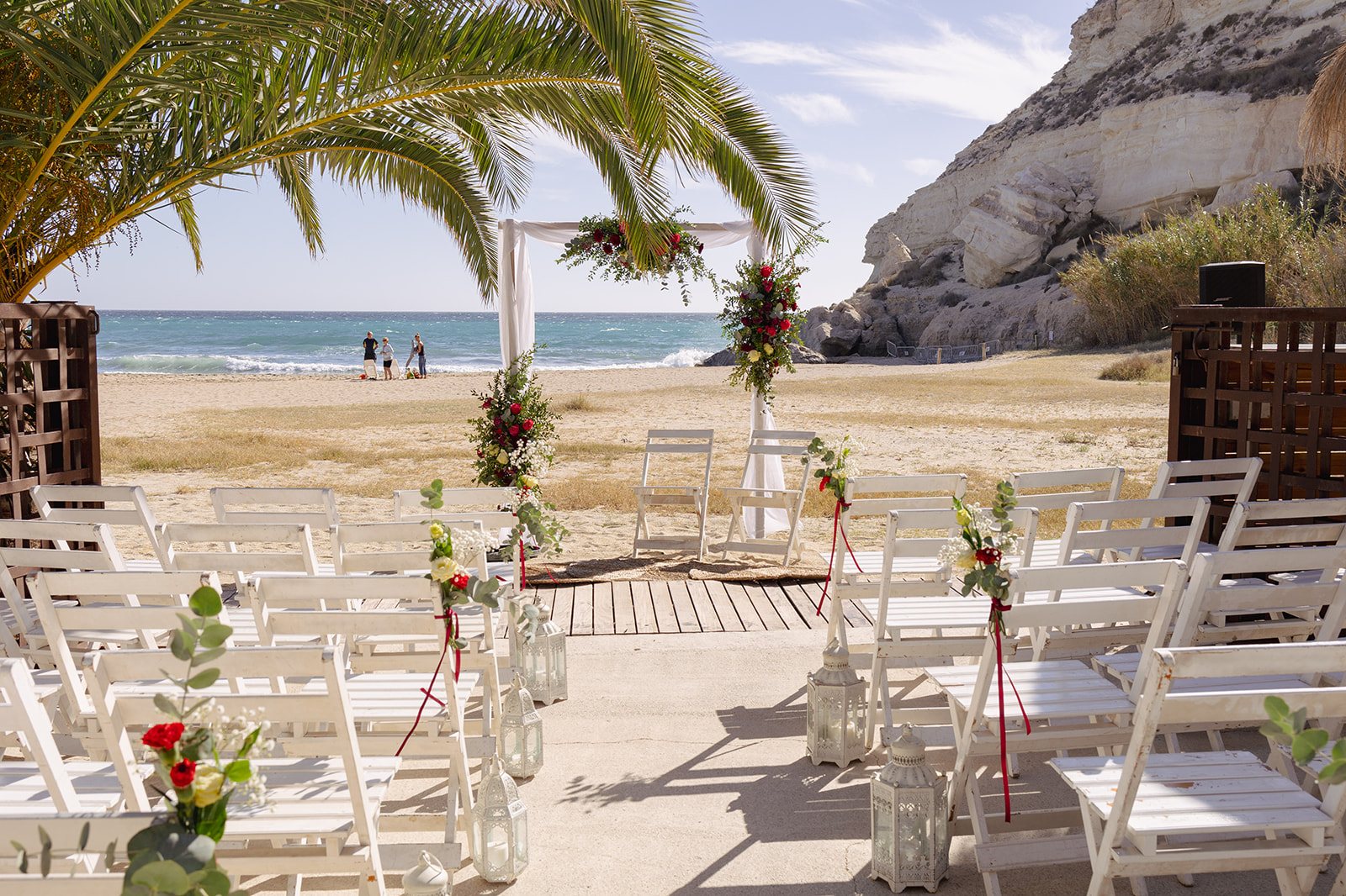 Traubogen mit roten und weißen Blumen im Sand am Strand von Agua Amarga, dahinter Kliff und Meer