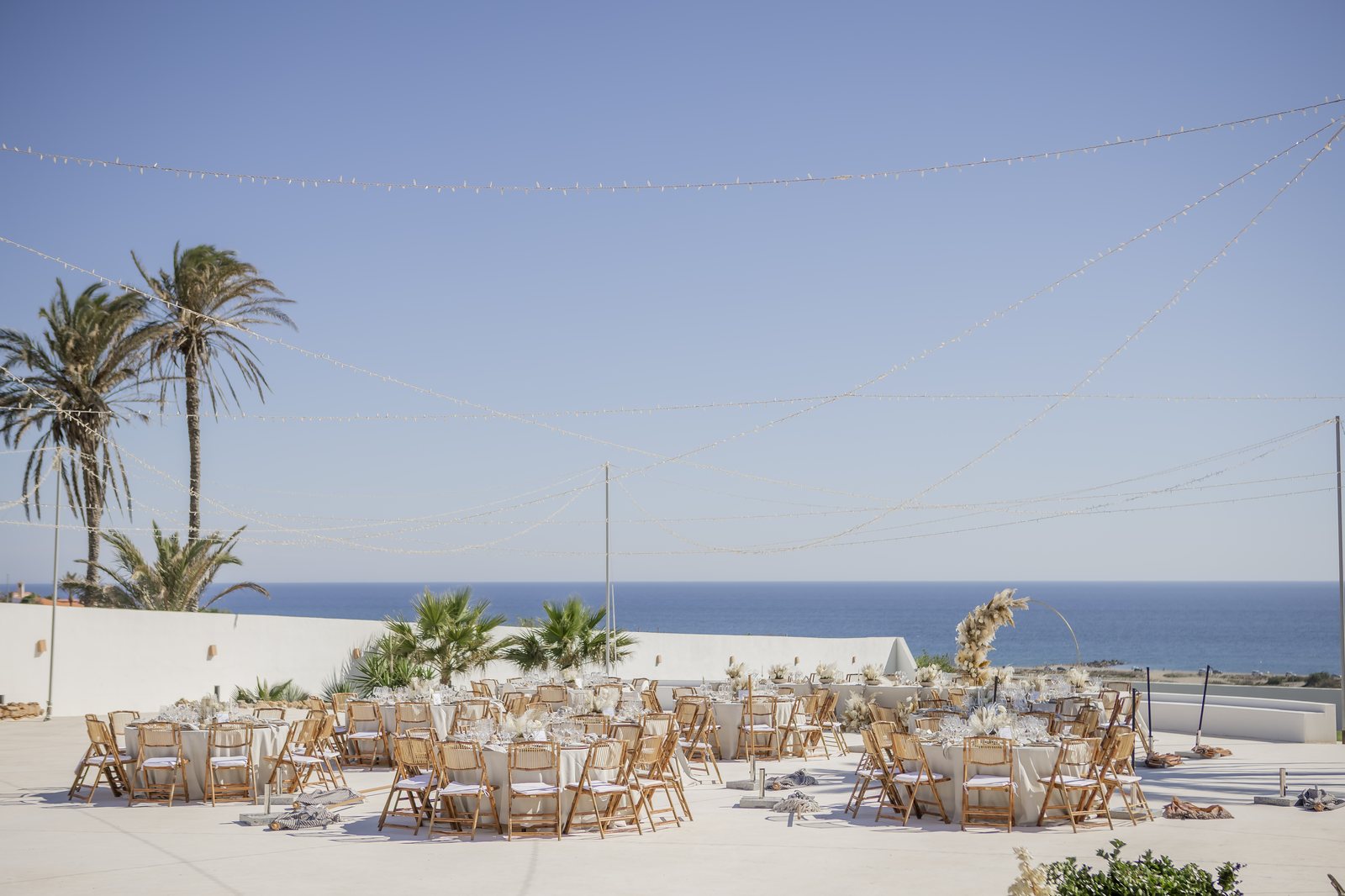 Runde Hochzeitstische zwischen Palmen mit Blick aufs Meer, weiße Feier-Location bei Guardias Viejas in Almería