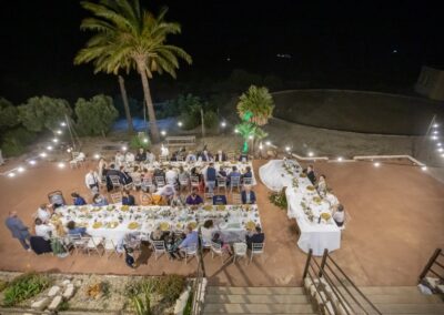 Hochzeitstafeln auf der Terrasse in der Abenddämmerung, Lichterketten zwischen den Palmen