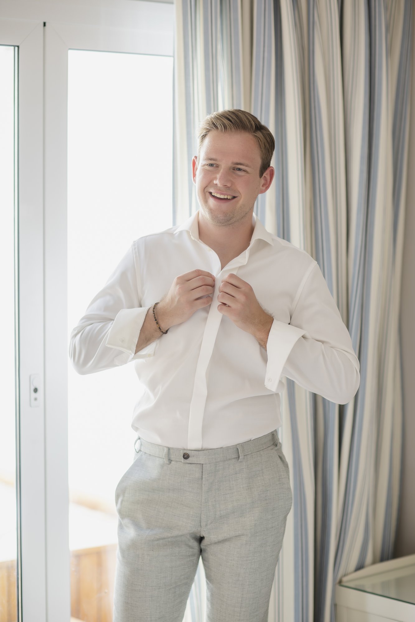 Groom buttoning his shirt, getting ready, wedding Agua Amarga