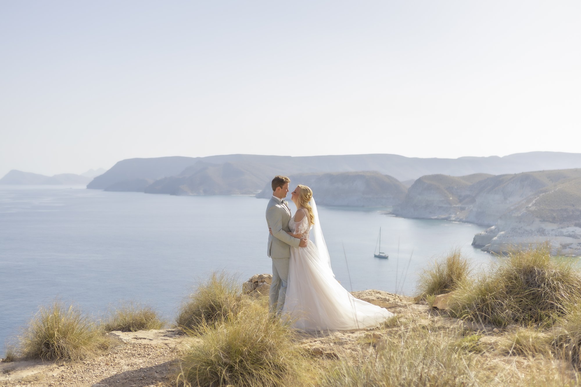Couple on the cliff with sailing boats in the bay, wedding Agua Amarga