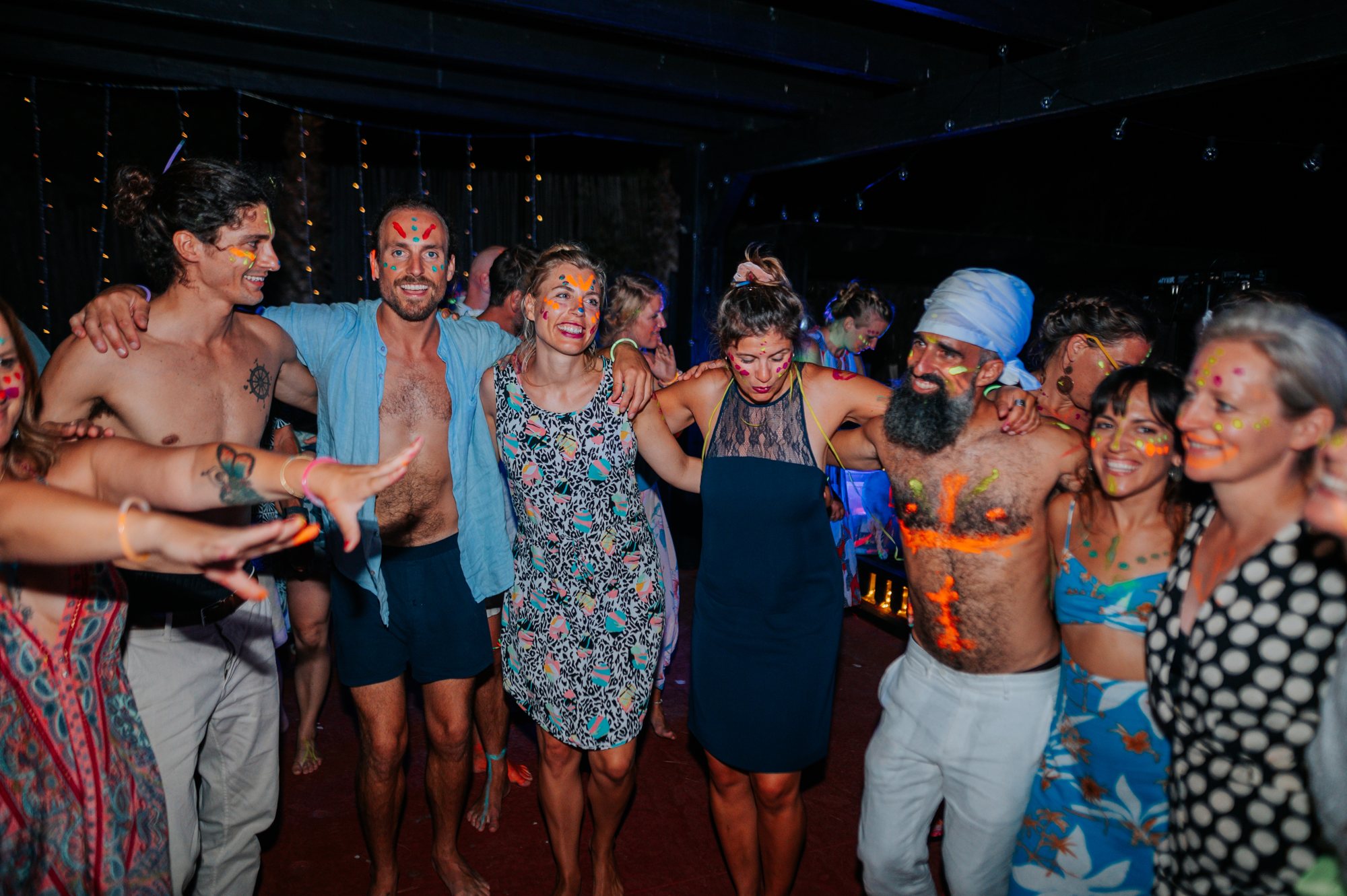 Gäste tanzen Arm in Arm mit Neonfarben, Hochzeit am Meer